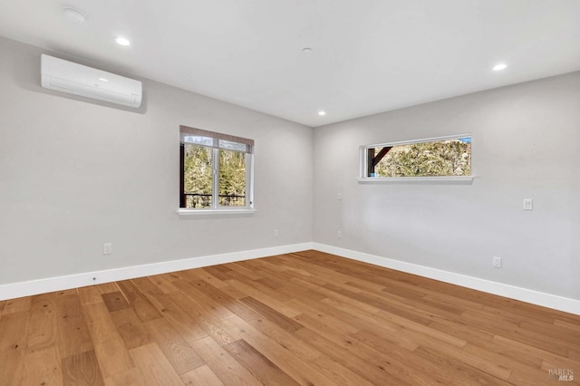 empty room with light wood-style floors, recessed lighting, a wall unit AC, and baseboards