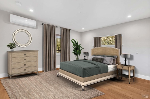 bedroom featuring a wall unit AC, light wood finished floors, and multiple windows