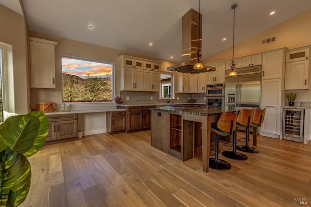 kitchen featuring beverage cooler, island range hood, glass insert cabinets, a center island, and hanging light fixtures