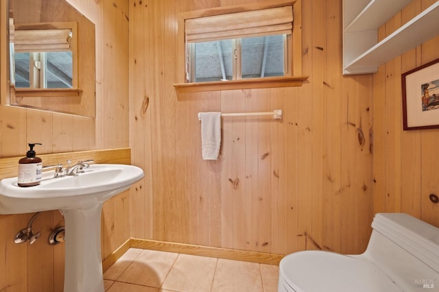 half bath with tile patterned flooring, a sink, wooden walls, and toilet