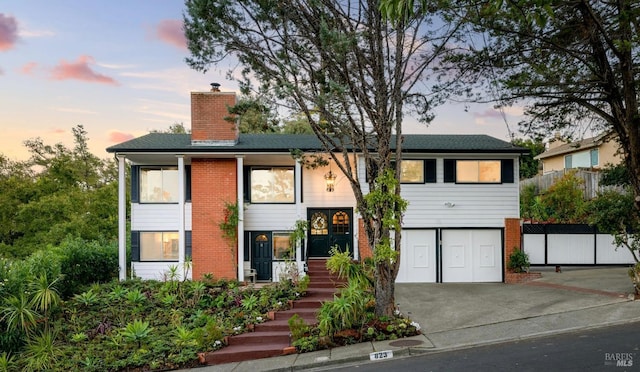 view of front of property featuring a garage, concrete driveway, brick siding, and a chimney