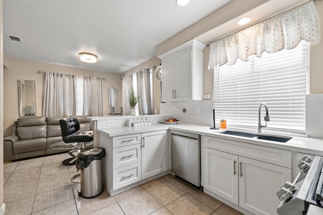 kitchen with dishwasher, kitchen peninsula, sink, light tile patterned floors, and white cabinetry