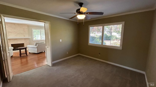 empty room with ceiling fan, carpet, a large fireplace, and ornamental molding