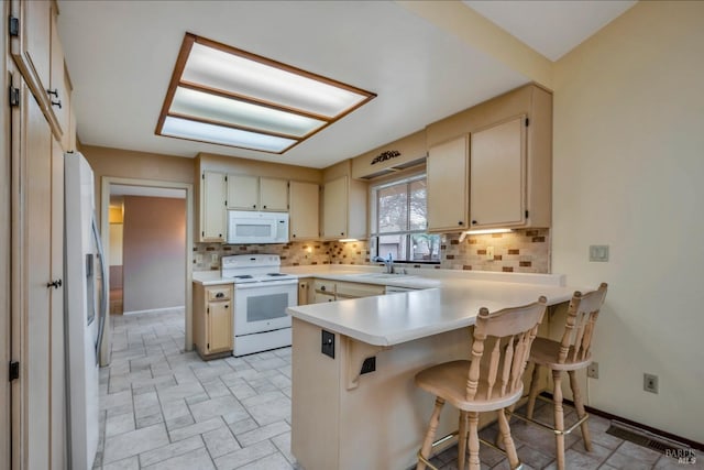 kitchen featuring kitchen peninsula, sink, cream cabinetry, white appliances, and a breakfast bar area