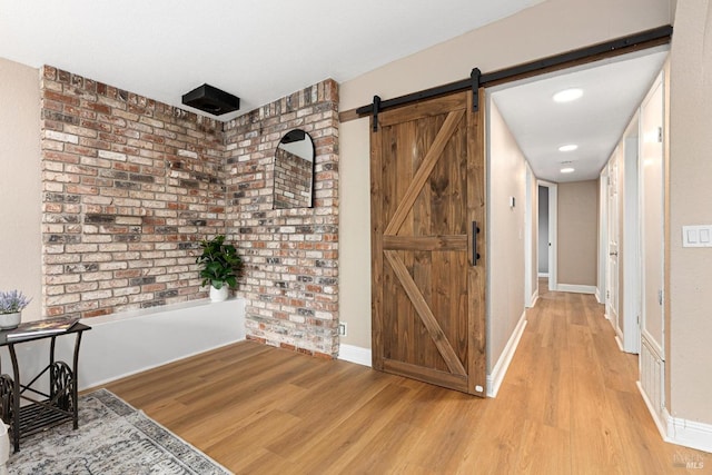 corridor featuring light wood-style flooring, recessed lighting, a barn door, and baseboards