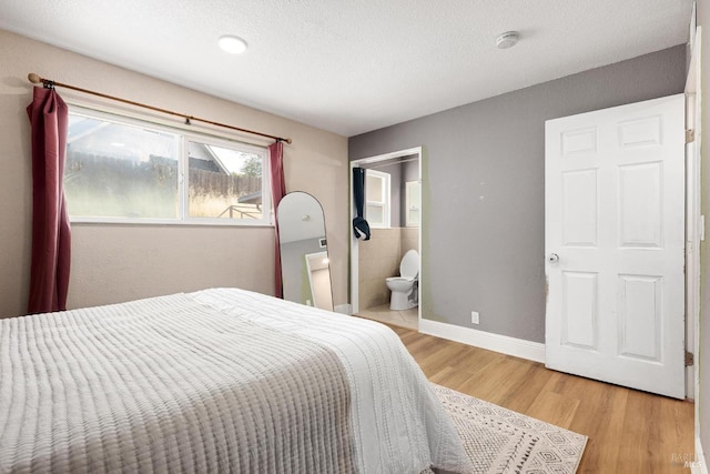 bedroom with light wood-type flooring, a textured ceiling, and ensuite bath