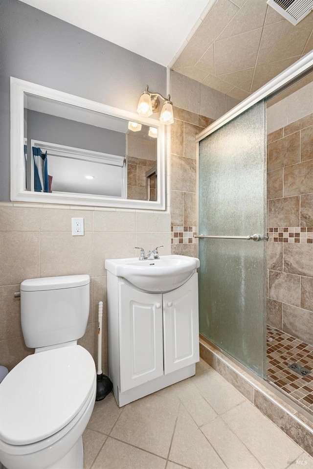 bathroom with tile patterned floors, a shower with shower door, tile walls, and vanity