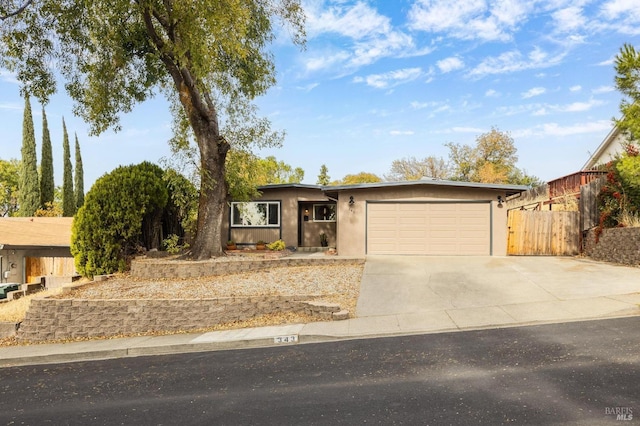 ranch-style house featuring an attached garage, concrete driveway, stucco siding, and fence