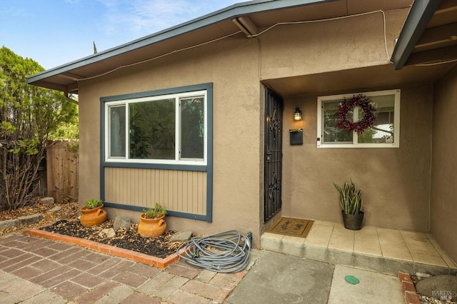 view of exterior entry featuring stucco siding and fence