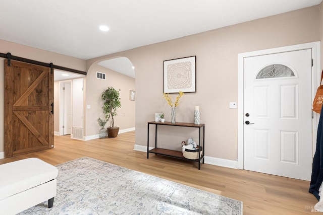 foyer entrance featuring light wood-style floors, baseboards, visible vents, and arched walkways