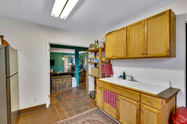 kitchen featuring a textured ceiling, stainless steel refrigerator, dark tile patterned floors, and sink