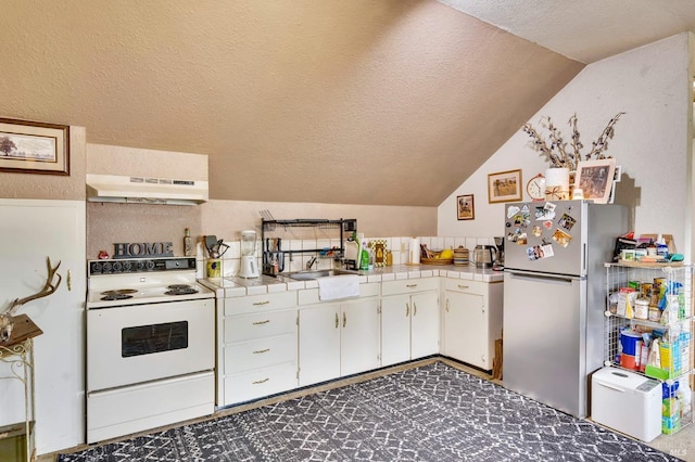 kitchen with electric stove, tile countertops, white cabinetry, stainless steel refrigerator, and lofted ceiling