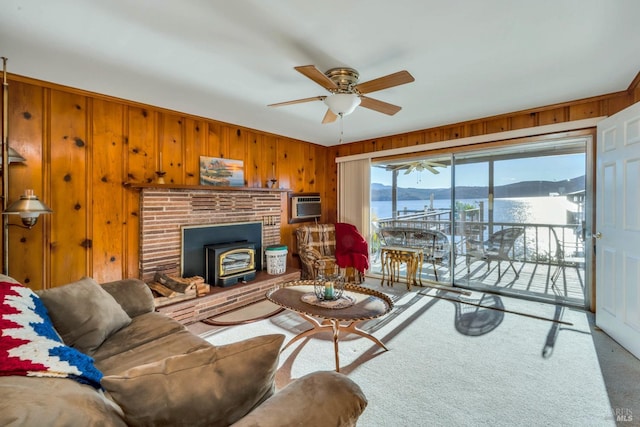 carpeted living room with a wood stove, a wall mounted AC, wood walls, a water and mountain view, and ceiling fan