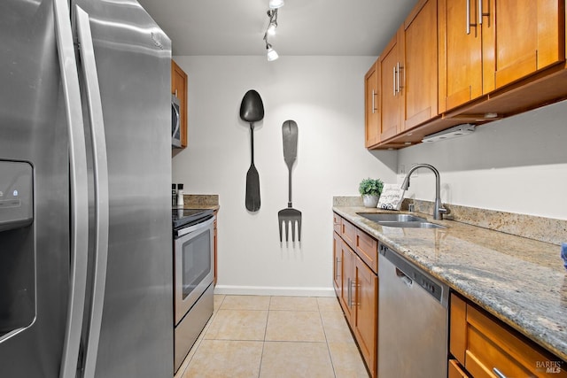 kitchen with appliances with stainless steel finishes, track lighting, light stone counters, sink, and light tile patterned flooring