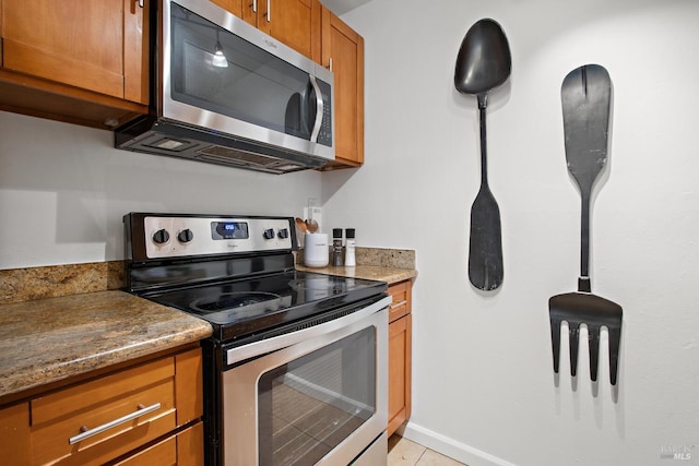 kitchen with light tile patterned floors, hanging light fixtures, appliances with stainless steel finishes, and dark stone counters