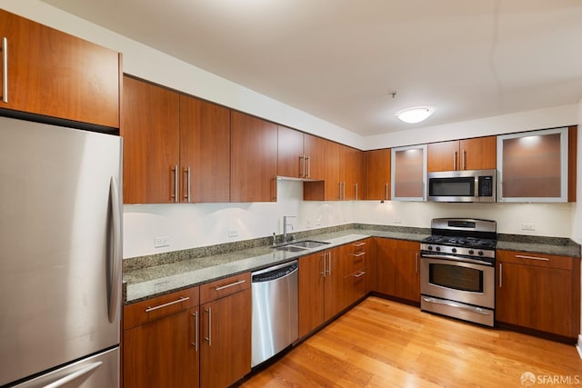 kitchen featuring dark stone countertops, stainless steel appliances, sink, and light wood-type flooring