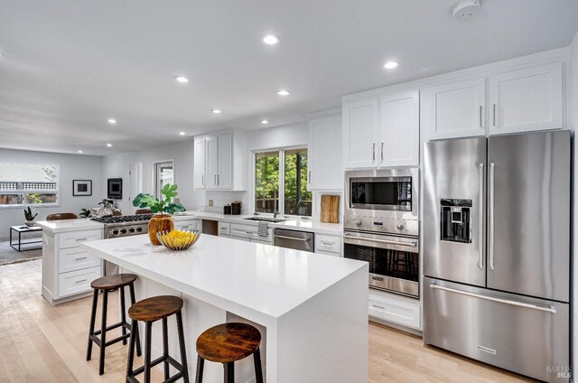 kitchen featuring white cabinetry, light wood-type flooring, a center island, appliances with stainless steel finishes, and a kitchen breakfast bar