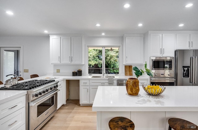 kitchen with sink, high end appliances, white cabinetry, a kitchen breakfast bar, and light hardwood / wood-style floors