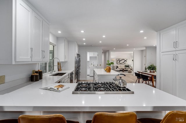 kitchen featuring kitchen peninsula, stainless steel appliances, sink, white cabinets, and a breakfast bar area