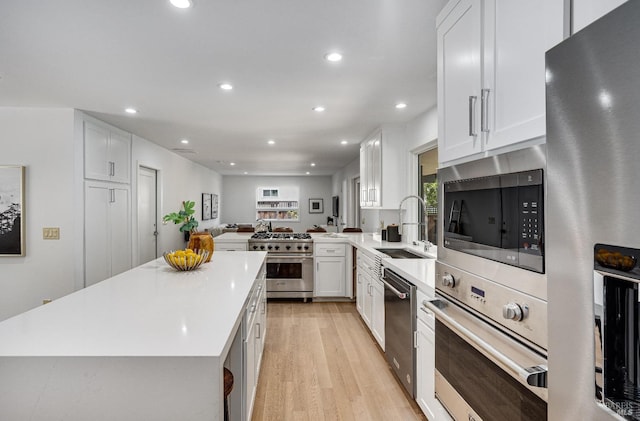 kitchen featuring appliances with stainless steel finishes, sink, light hardwood / wood-style flooring, kitchen peninsula, and white cabinets