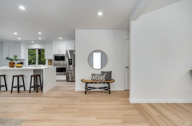 kitchen with white cabinetry, appliances with stainless steel finishes, a kitchen breakfast bar, and light hardwood / wood-style flooring