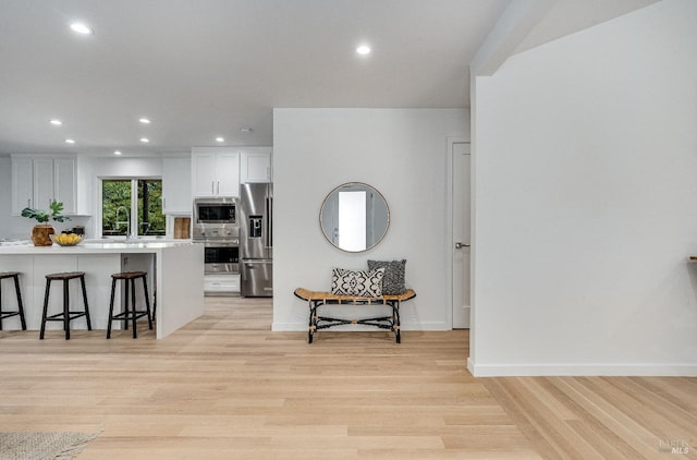 kitchen with a breakfast bar area, light wood-type flooring, stainless steel appliances, white cabinets, and sink