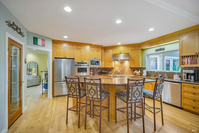 kitchen featuring a center island, backsplash, appliances with stainless steel finishes, light hardwood / wood-style floors, and a breakfast bar area