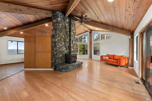 unfurnished living room with wood ceiling, beamed ceiling, light hardwood / wood-style floors, a wood stove, and ceiling fan