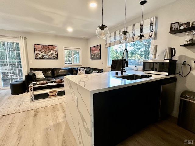 kitchen featuring stainless steel microwave, pendant lighting, light stone counters, wood finished floors, and a sink