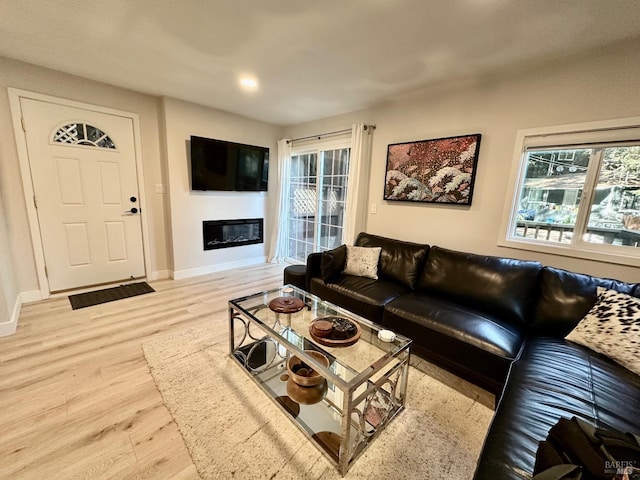 living area featuring a wealth of natural light, a glass covered fireplace, baseboards, and wood finished floors