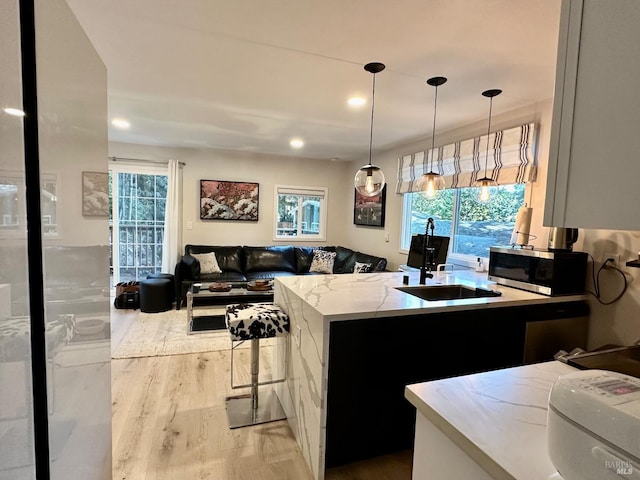 kitchen featuring wood finished floors, light stone countertops, pendant lighting, stainless steel microwave, and open floor plan