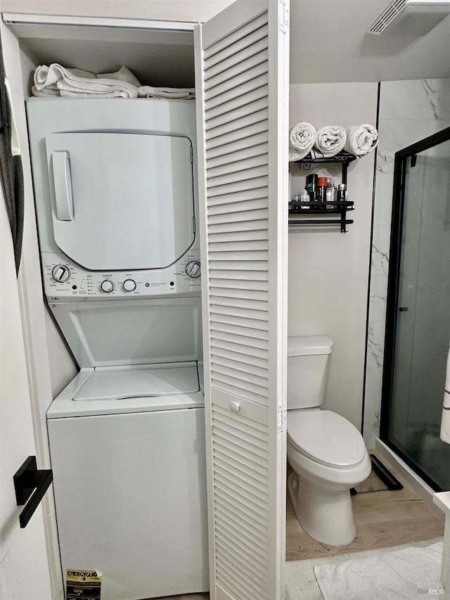 laundry area with laundry area, wood finished floors, and stacked washer / drying machine