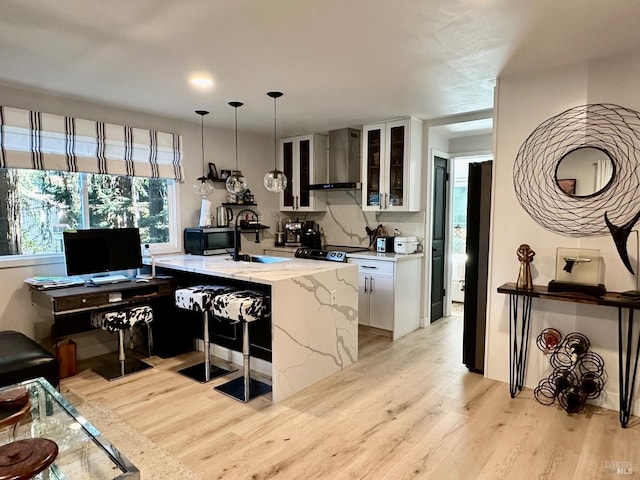 kitchen featuring a sink, light wood-type flooring, white cabinetry, and wall chimney range hood