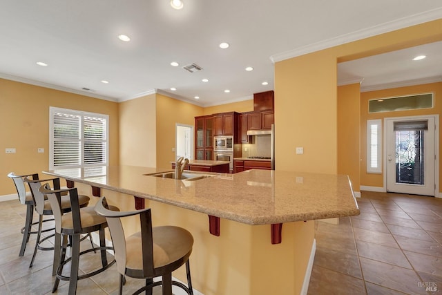 kitchen featuring visible vents, appliances with stainless steel finishes, ornamental molding, a sink, and a large island with sink