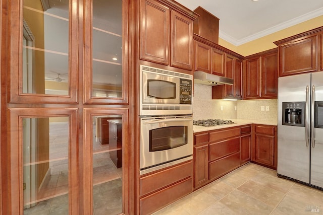 kitchen with crown molding, light countertops, stainless steel appliances, under cabinet range hood, and glass insert cabinets