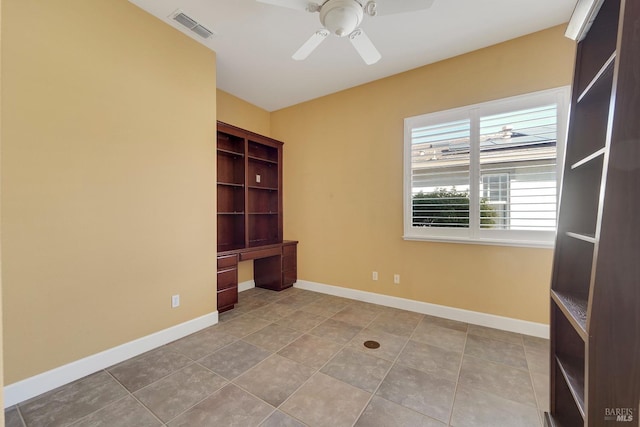 tiled empty room featuring visible vents, ceiling fan, built in desk, and baseboards