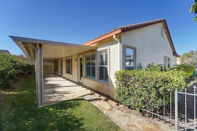 view of home's exterior with a patio, a lawn, a tiled roof, and stucco siding