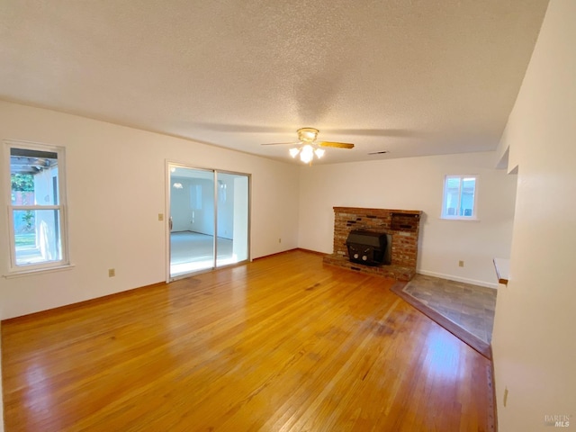 unfurnished living room featuring wood-type flooring, a brick fireplace, ceiling fan, and a textured ceiling