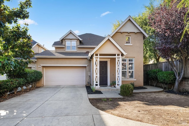 traditional-style home with stucco siding, fence, roof with shingles, concrete driveway, and a garage