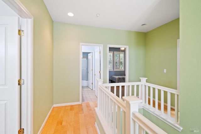 corridor with light wood finished floors, baseboards, an upstairs landing, and recessed lighting