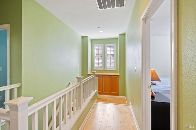 hallway featuring an upstairs landing, light wood-type flooring, and a textured wall