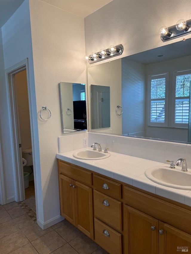bathroom with tile patterned floors, double vanity, toilet, and baseboards