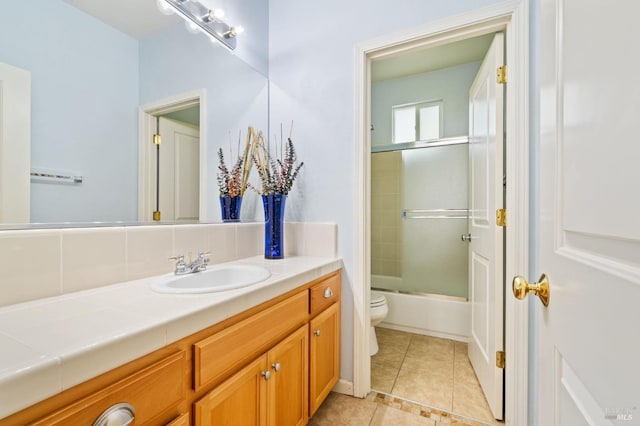 bathroom featuring toilet, vanity, tile patterned flooring, and bath / shower combo with glass door