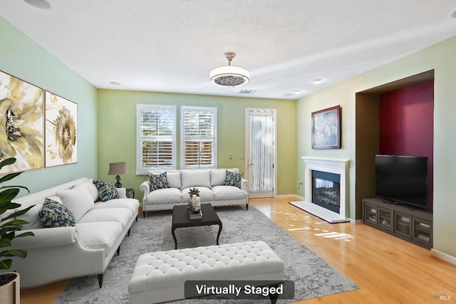 living area with wood finished floors, a glass covered fireplace, and baseboards