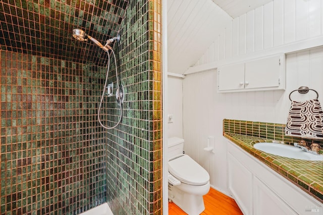 bathroom featuring tiled shower, vanity, wood walls, hardwood / wood-style flooring, and toilet