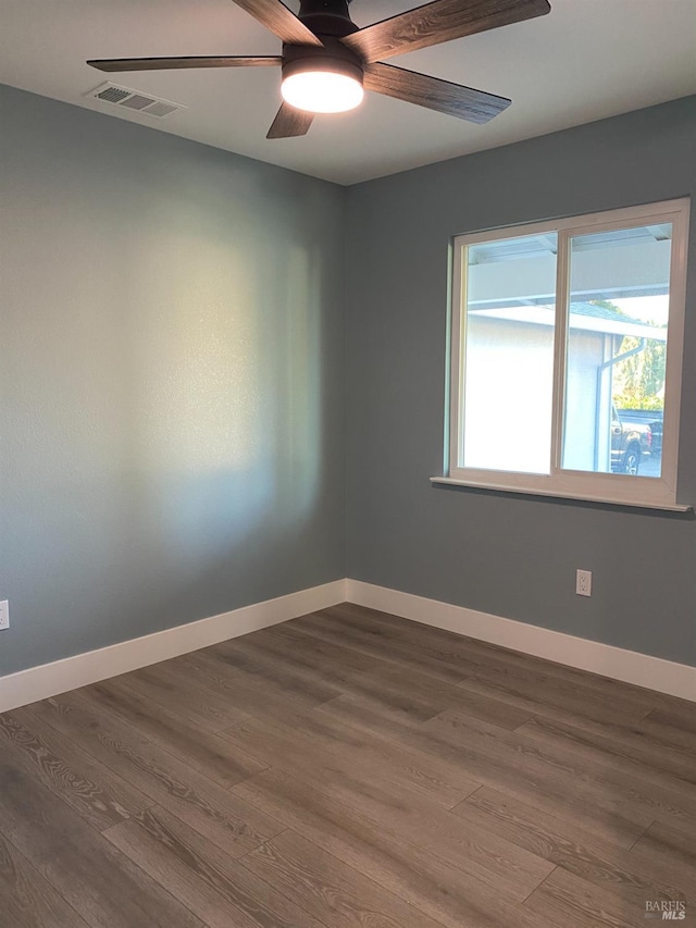 spare room featuring dark wood-style flooring, ceiling fan, visible vents, and baseboards