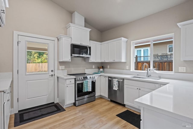 kitchen with stainless steel appliances, vaulted ceiling, white cabinets, sink, and light wood-type flooring