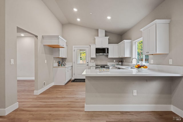 kitchen with white cabinets, kitchen peninsula, stainless steel appliances, and vaulted ceiling