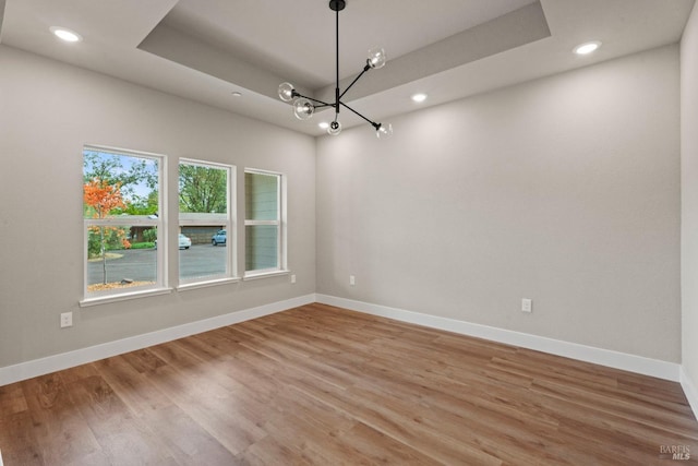 spare room featuring wood-type flooring, an inviting chandelier, and a tray ceiling