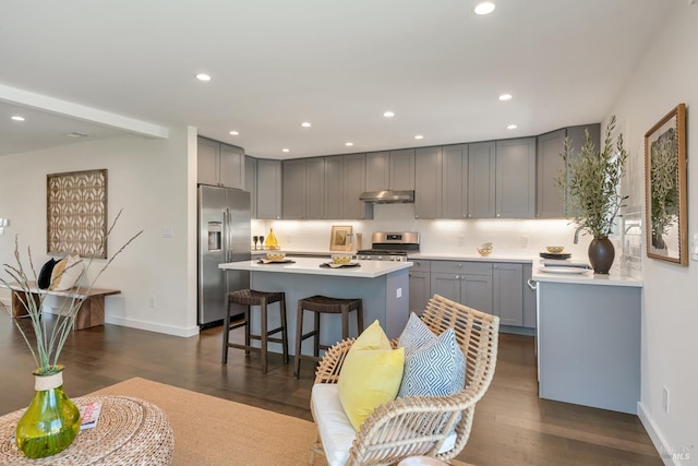 kitchen featuring a kitchen bar, dark hardwood / wood-style flooring, gray cabinets, a kitchen island, and appliances with stainless steel finishes